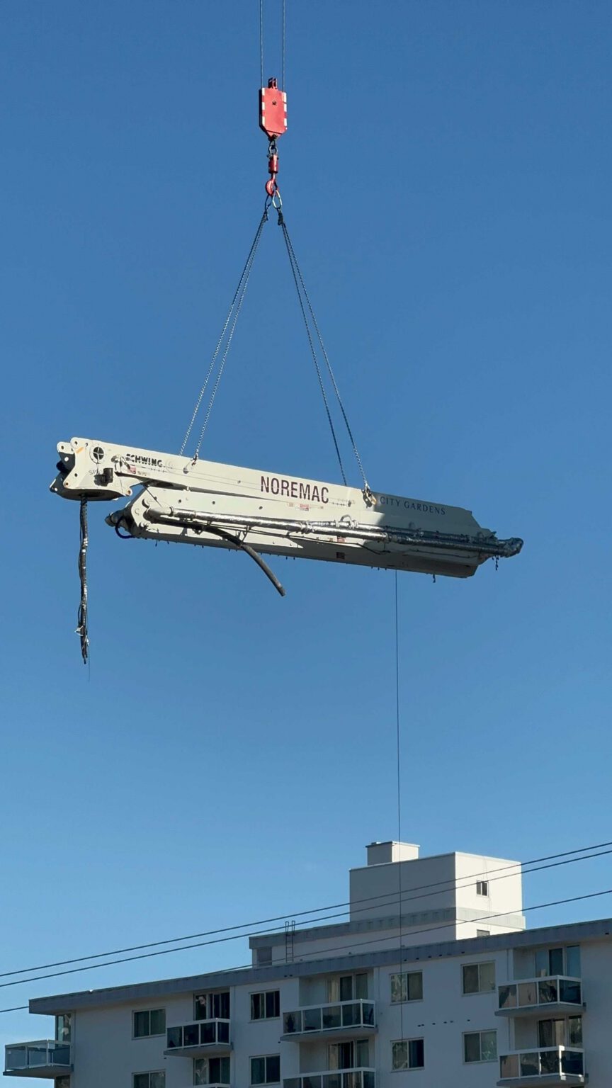 A Noremac placing boom attached to a crane, dangling high above an apartment building.
