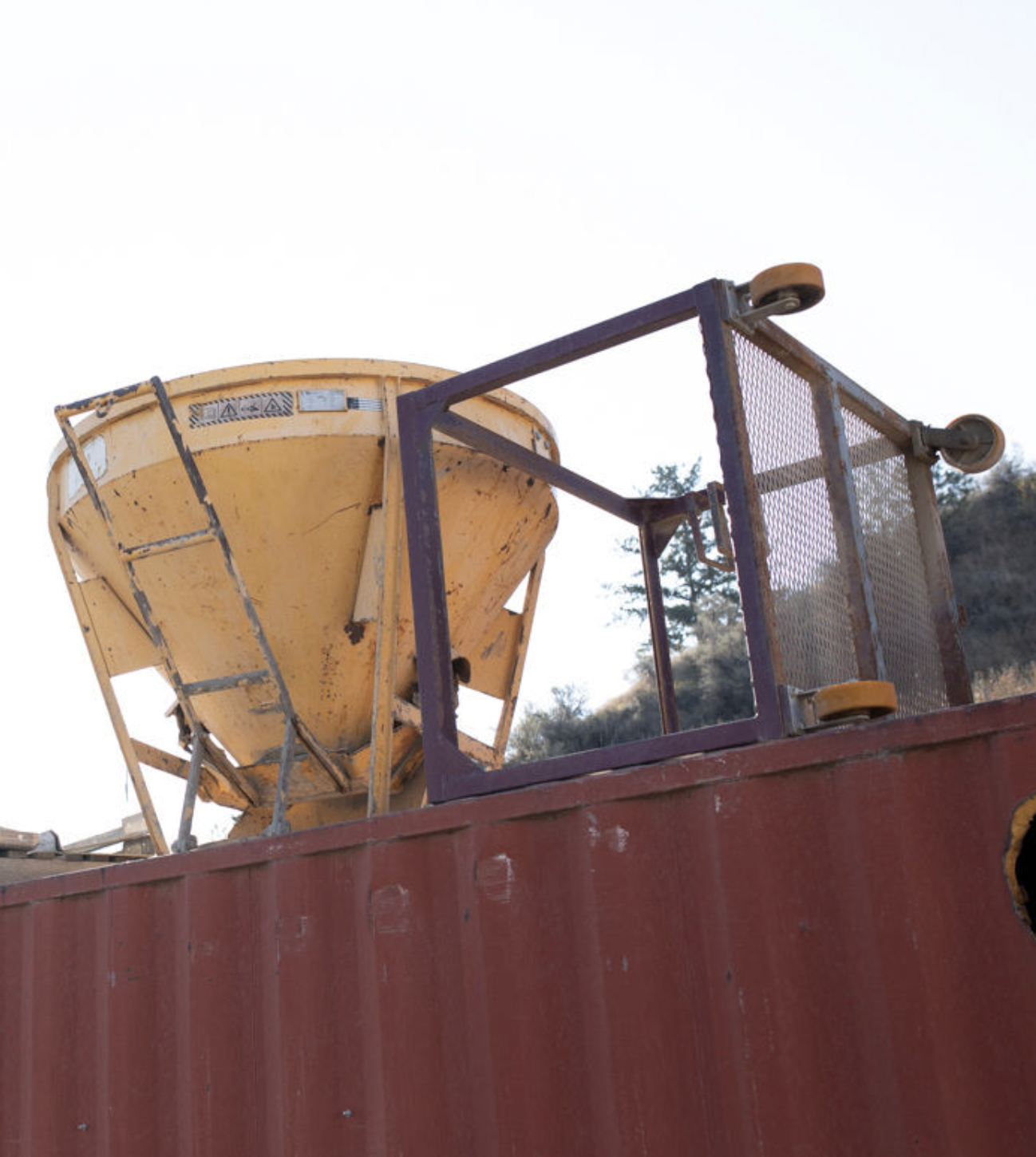 A yellow concrete bucket atop a maroon bin. Noremac offers concrete bucket rentals!