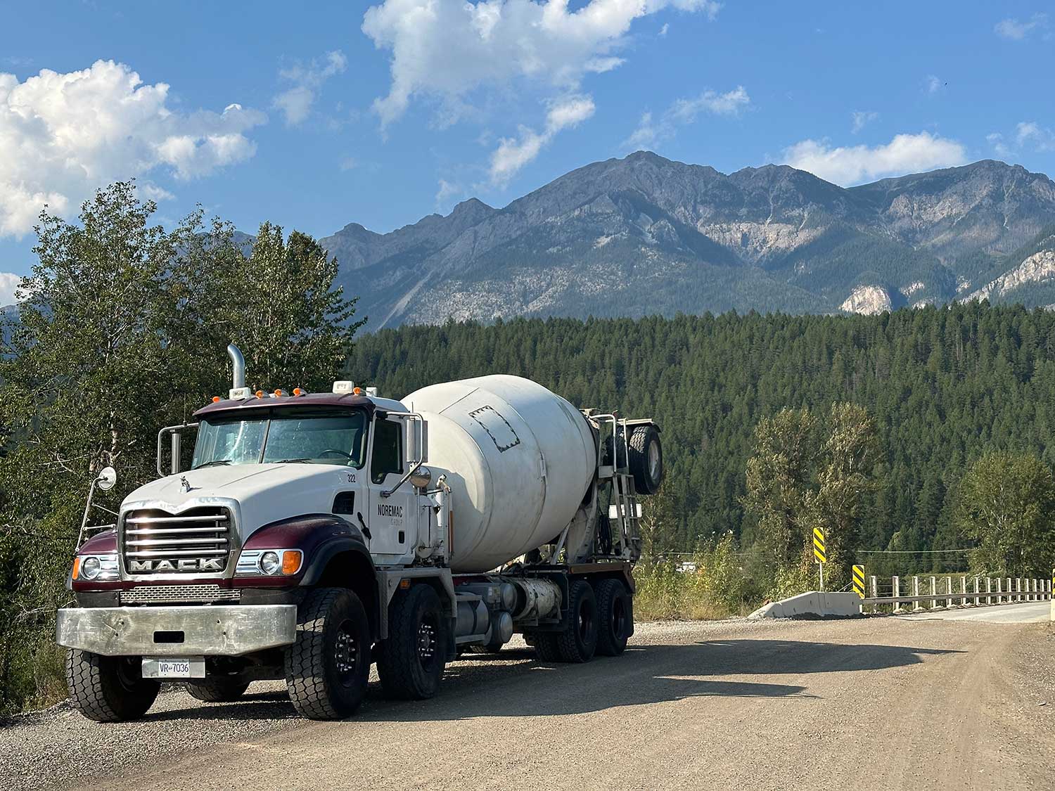 A Noremac branded MACK truck outfitted with a construction mixer. Mountains and blue sky in the background.