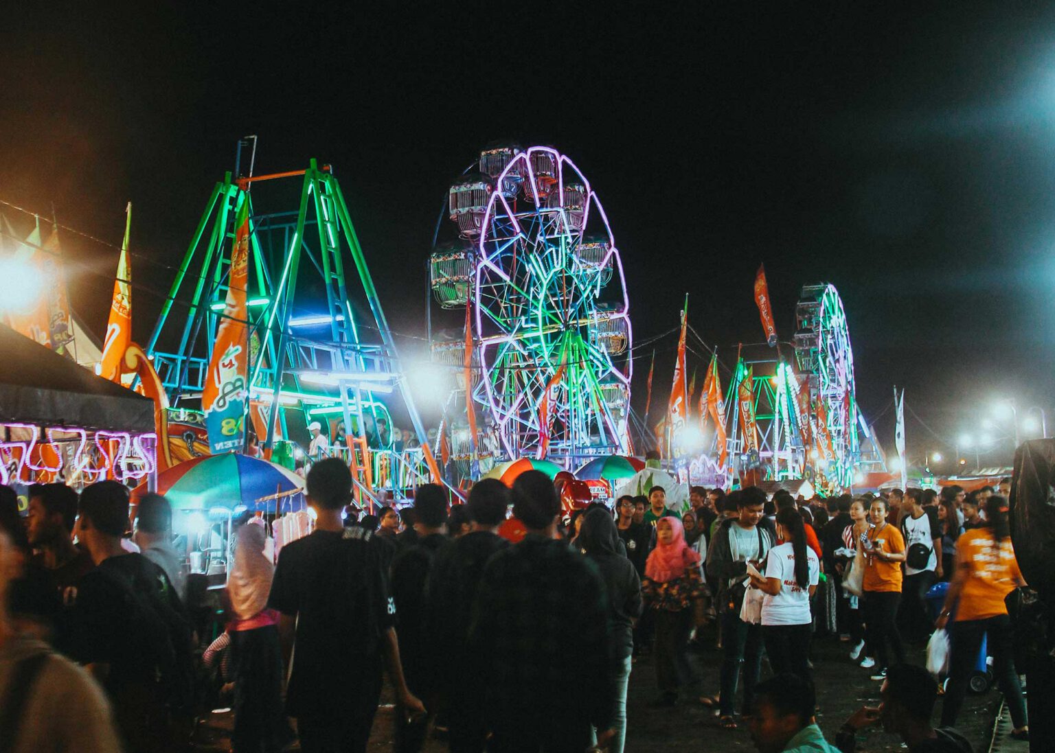 A fairground at night time, neon lights and crowds all around.