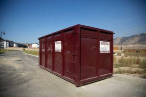A burgundy Noremac disposal bin, a blue sky in the background.