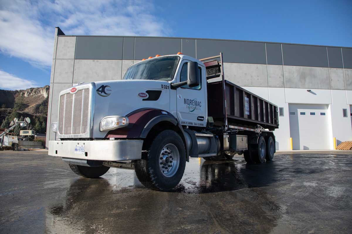 A roll-off bin truck with the Noremac logo on the side.
