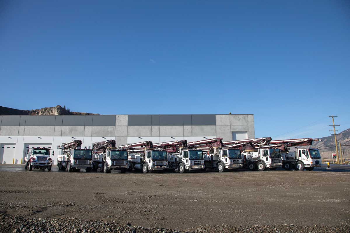 A distant shot of boom pumps lined up in front of an industrial building, blue sky all around.
