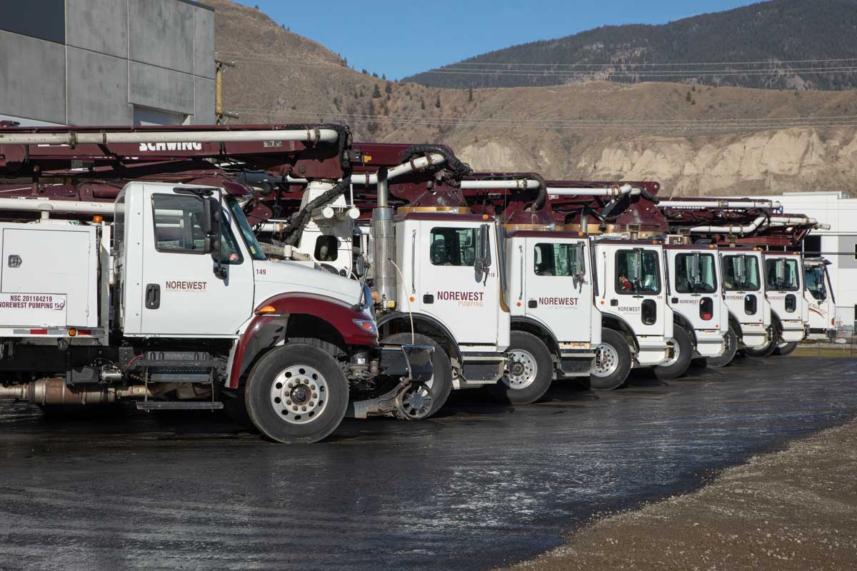 Boom pumps are lined up on a concrete tarmac.
